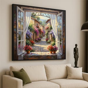 May include: A framed painting showing an Italian street scene through an open window. The artwork features a cobbled path flanked by buildings decorated with colourful flowers. Two pots of red flowers sit on the window ledge, with white curtains framing the view.