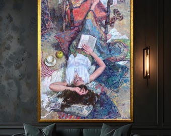 May include: An oil painting in a gold frame depicts a person reclining on pillows and reading a book. The artwork features a white blouse, a green apple, and a teacup. The color palette includes blues, reds, and greens.
