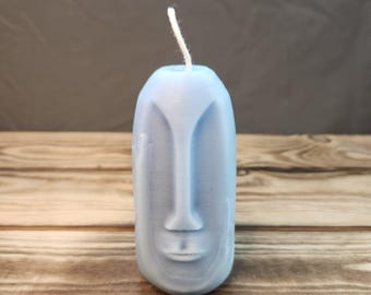 May include: A blue candle shaped like a face with a white wick. The candle is on a wooden surface.