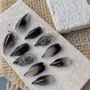 May include: A set of ten almond-shaped press-on nails featuring a gradient design that transitions from clear to black. Some nails display a solid black finish, while others incorporate speckled or mottled black and gray patterns across the surface.