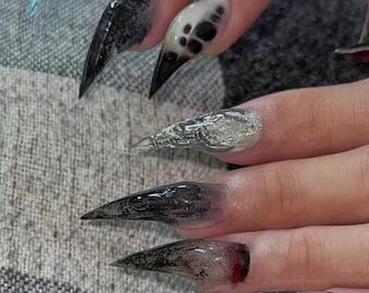 Könnte beinhalten: Nahaufnahme von langen, spitzen, schwarz-weißen Nägeln mit einem klaren, glitzernden Finish. Die Nägel sind in einer scharfen, krallenartigen Form gestylt.