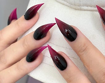 May include: Stiletto-shaped press-on nails featuring a dark gradient design that transitions from a deep black base to a vibrant magenta tip. The glossy finish includes small, clear water droplet accents on the surface of each nail.