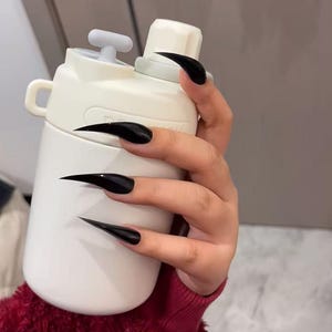 Könnte beinhalten: Eine matte, cremeweiße Trinkflasche mit zylindrischem Körper, einem sicheren Schraubverschluss mit kleinem grauen Kippschalter und einer seitlichen Schlaufe zum Tragen. Die Flasche hat eine glatte Oberfläche und eine robuste Konstruktion.