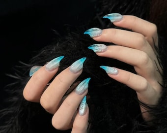 May include: Close-up of hands with long, pointed, blue and silver glitter ombre nails.