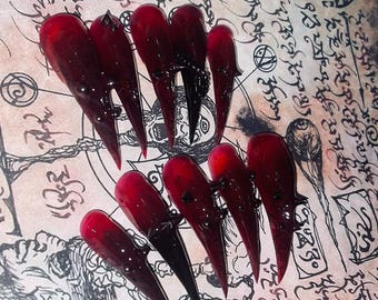 May include: Set of long, pointed, red and black false nails with a dripping blood effect.