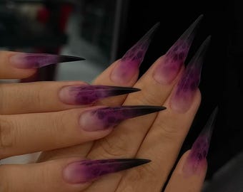 May include: Long, pointed, clear acrylic nails with a black ombre fade and a purple marbled design.