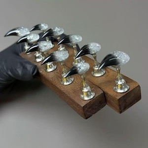 May include: A collection of silver and black nail art pieces, each with a glittery, rounded top and a pointed, black tip. The nails are mounted on a wooden base, showcasing a unique and artistic design.