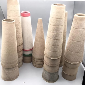 May include: A collection of various-sized, cone-shaped paper yarn cones. Some cones are plain, while others have colored bands of red and green. The cones are made of a light brown, textured paper material.