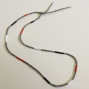 May include: A gray string necklace with red, black, and white beads.