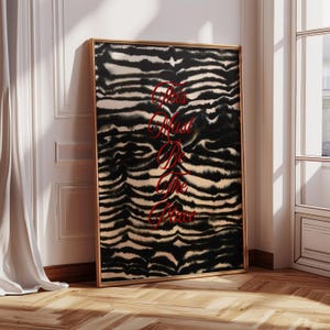 Op de afbeelding: Een ingelijste kunstafdruk met een zwart-wit zebra streepjespatroon. Het kunstwerk bevat de rode tekst "This Must Be The Place". De lijst is goudkleurig en de afdruk leunt tegen een witte muur en een houten vloer.