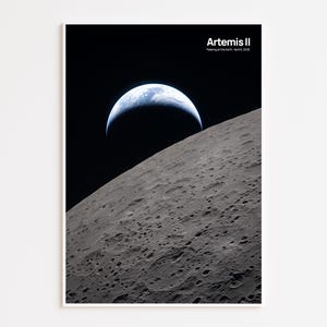 May include: A framed print showing the Earth rising over the Moon's surface. The image depicts the Earth as a blue and white crescent against a black sky, with the gray, cratered surface of the moon in the foreground. The text "Artemis II" is at the top.