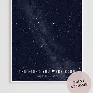 Peut inclure: Impression encadrée représentant un ciel nocturne bleu foncé parsemé de nombreuses étoiles blanches et une voie lactée. Le texte "THE NIGHT YOU WERE BORN" est affiché en bas, avec les détails de la date et de l'heure. Un cercle rose avec le texte "PRINT AT HOME!" est en bas à droite.
