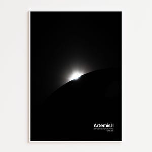 May include: A framed print featuring a celestial event. The image shows a bright light emerging from behind a dark, curved shape, possibly a planet or moon. The text "Artemis II" is at the bottom, along with additional details.