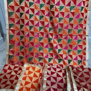 Peut inclure: Un ensemble de trois carrés de tissu brodés de couleurs vives avec des motifs géométriques dans des tons de rouge, orange, vert et rose. Le tissu est bordé d'un galon de fil doré.