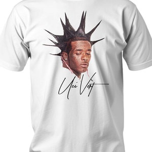 Puede incluir: Camiseta blanca con un retrato de una persona con pelo puntiagudo y una firma. El retrato está en tonos marrones y rojos. La firma está en cursiva negra. La camiseta es de cuello redondo clásico.