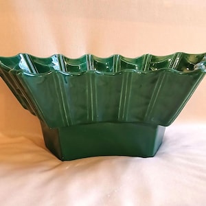 May include: A large, green ceramic bowl with a fluted rim and a geometric base. The bowl is made of glazed pottery and has a smooth, glossy finish.