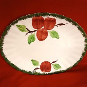 May include: Oval serving platter with a white center and a green, scalloped edge. The platter features a hand-painted design of red apples, green leaves, and brown branches. A decorative piece for serving food.