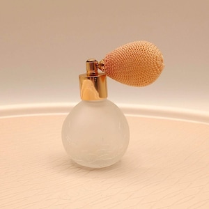 May include: A vintage perfume atomizer with a frosted glass bottle and a gold-colored metal top. The atomizer has a peach-colored bulbous spray. The bottle has a delicate floral design etched into the glass.