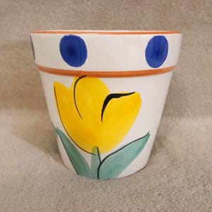 May include: White ceramic flower pot with a yellow tulip and blue polka dots around the rim.