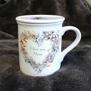 May include: White ceramic mug with a floral heart design and the text "I love you, Mom".