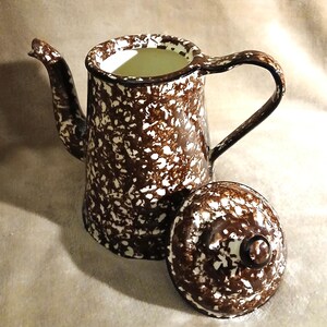 May include: A brown and white speckled enamel coffee pot with a lid. The pot has a handle and a spout.