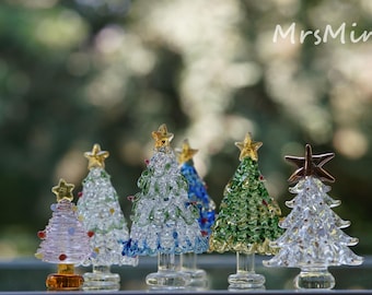 Peut inclure: Six petits sapins de Noël en verre de différentes couleurs, dont transparent, vert, bleu et rose. Chaque sapin est surmonté d'une étoile dorée et décoré de petites perles de verre.