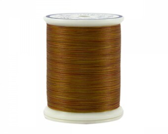 May include: A spool of brown thread with a white label. The thread has a subtle shimmer and is wound tightly on the spool.