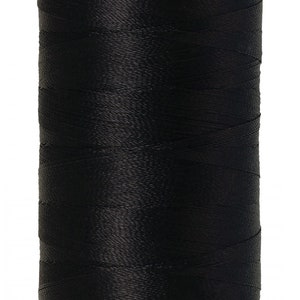 Puede incluir: Un carrete de hilo negro Mettler poly sheen. El carrete tiene una parte superior e inferior blancas con el nombre de la marca y la información del producto. Las palabras "GERMAN MADE" están impresas en la parte inferior.