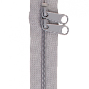 Puede incluir: Una cremallera gris con dos tiradores. La cremallera está cerrada y los tiradores están en la posición superior.