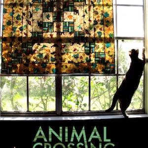 Pode incluir: Uma colcha com um padrão colorido de cruzamento de animais está pendurada em uma janela. Um gato preto está sentado em um parapeito da janela, olhando para fora. A colcha mede 44 polegadas por 44 polegadas. A colcha é feita por Cherry House Quilts.