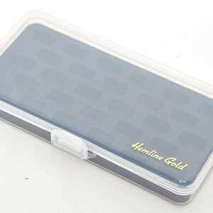 Könnte beinhalten: Eine transparente Plastik-Aufbewahrungsbox mit einem blauen Deckel. Der Deckel hat ein strukturiertes Muster und die Worte "Hemline Gold" in goldenen Buchstaben.