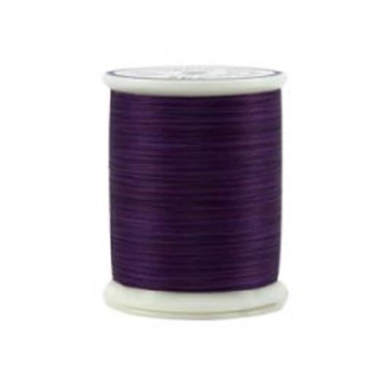 May include: A spool of deep purple thread wound on a white plastic bobbin.