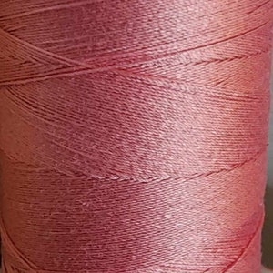 May include: A spool of pink thread, tightly wound and textured. The thread has a slight sheen, suggesting a smooth, high-quality material. The spool is cylindrical, with a white base.