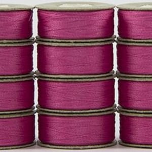 May include: A stack of 12 spools of pink thread, each spool is wrapped in a beige paper label.