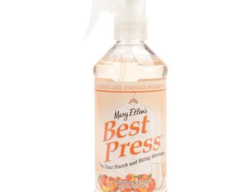 May include: A clear spray bottle of Mary Ellen's Best Press, a clear starch and sizing alternative. The bottle is labelled with a peach and cream design and the text "Peaches & Cream 16 fl oz (473 ml)".