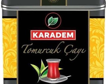 May include: A rectangular black metal tea tin featuring a central black panel with a red and white logo reading KARADEM, the text Tomurcuk Çayı, and an illustration of a glass of red tea with green tea leaves. The sides have yellow floral patterns.