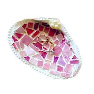 Op de afbeelding: Een roze en witte mozaïek schelp ringenschotel met twee gouden ringen en een parel accent.