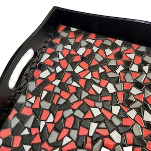May include: A black serving tray with a mosaic design. The mosaic is made of red, black, white, and gray tiles. The tray has a handle on one side.