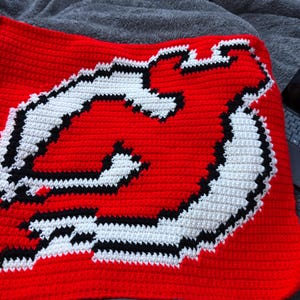May include: A red, white, and black crocheted blanket with a large, stylized letter "N" in the center.