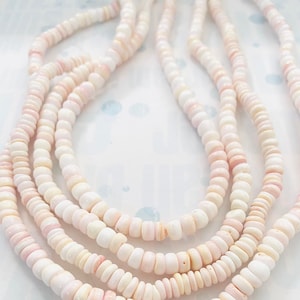 Peut inclure: Un collier à plusieurs rangs composé de petites perles circulaires en forme de disque dans des tons variés de rose pâle, crème et blanc. Les perles ont une texture lisse et polie et sont enfilées pour créer un aspect superposé en cascade.