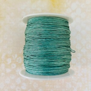 Könnte beinhalten: Eine Spule mit tealgrünem gewachstem Garn, fest auf einer weißen Kunststoffspule gewickelt.