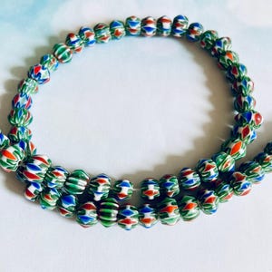 May include: Strands of colorful glass beads. The beads are a mix of red, white, blue, and green, with a ribbed texture. The beads are strung together, creating a necklace or bracelet.