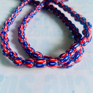 May include: A strand of red, white, and blue glass beads. The beads are oval shaped and have a striped pattern.
