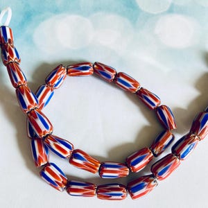 May include: Strands of colorful beads with a red, white, and blue striped pattern. The beads are strung together, creating a necklace or bracelet. The beads have a cylindrical shape and are arranged in a curved line.