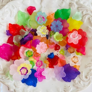 Puede incluir: Una colección de cuentas de plástico de colores en forma de flor y hoja. Las cuentas son translúcidas y tienen una variedad de colores, incluyendo rosa, morado, azul, verde, amarillo y naranja.