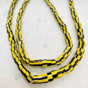 May include: A strand of black and yellow glass beads. The beads are cylindrical and have a checkerboard pattern.