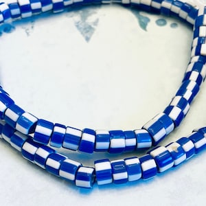 Puede incluir: Una hebra de cuentas de vidrio azul y blanco a cuadros. Las cuentas son cilíndricas y tienen un acabado brillante.