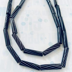 Può includere: Una collana di perline di vetro a strisce bianche e nere. Le perline sono cilindriche e hanno un design attorcigliato.