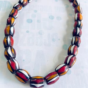 May include: A necklace featuring oval-shaped beads in a variety of colors. The beads are primarily red, white, yellow, and brown, with a striped pattern. The necklace is strung together, creating a loop.