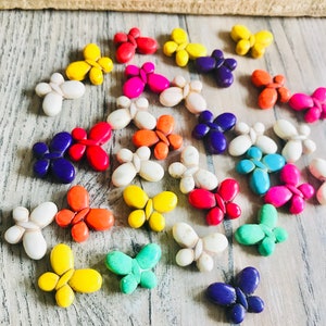 Könnte beinhalten: Sortiment an bunten, schmetterlingsförmigen Perlen aus Türkis. Die Perlen sind in verschiedenen Farben, darunter Blau, Grün, Gelb, Orange, Rot, Pink und Weiß.